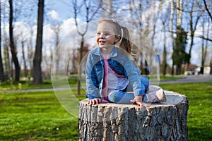 Little girl sitting on a stump in the park