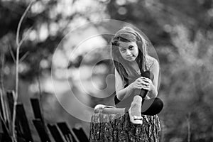 Little girl sitting on a stump in the village. Black and white photo.