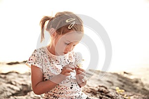 Little girl sitting on a sunlit beach at sunset, playing