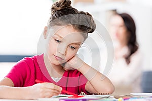 Little girl sitting at table and drawing with pen