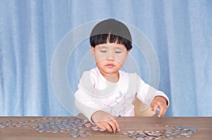 Little girl sitting at the table is playing with dollar coins on the table