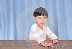 Little girl sitting at the table is playing with dollar coins on the table