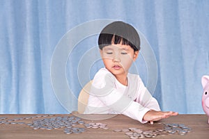 Little girl sitting at the table is playing with dollar coins on the table