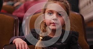 Little girl is sitting in the theater waiting for the performance