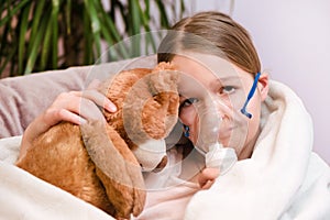 Little girl Sitting with a toy on the couch in a mask for inhalations, making inhalation with nebulizer at home inhaler