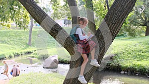 a little girl sitting on a tree branch in the park or in the backyard and drawing in a notebook. An introverted child