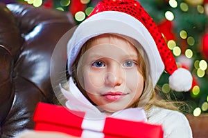 Little girl sitting by the tree holding a Christmas gift In the