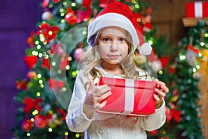 Little girl sitting by the tree holding a Christmas gift In the