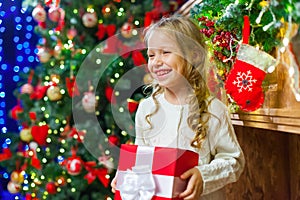 Little girl sitting by the tree holding a Christmas gift a lot o