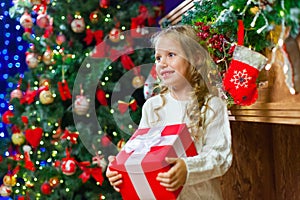 Little girl sitting by the tree holding a Christmas gift a lot o