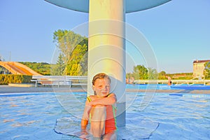 Little girl sitting under a sprinkler, shower in swimming pool. Portrait of little cute girl in the swimming pool. Sunny summer da