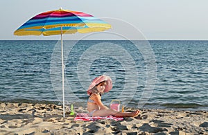 Little girl sitting under sunshade on beach