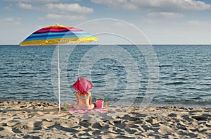 Little girl with sitting under sunshade on beach photo