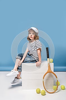 Little girl sitting on white boxes with tennis raquet and balls