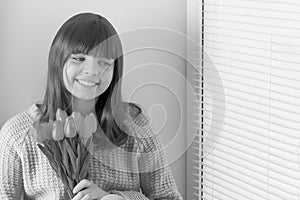 A little girl is sitting on the windowsill with a bouquet of tul