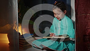 Little girl is sitting on windowsill, reading book