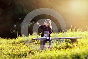 Little girl sitting on a wooden bench blows bubbles