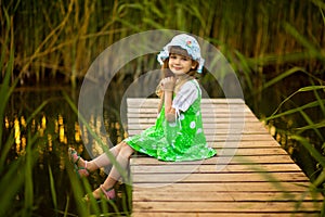 Little girl sitting on wooden bridge across river