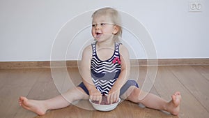 Little girl sitting on a wooden floor eating a ripe red raspberries