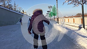 A little girl skates on ice in winter. Back view. Outdoors handheld shot.