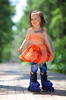 Little girl in skirt roller-blades and smiles in