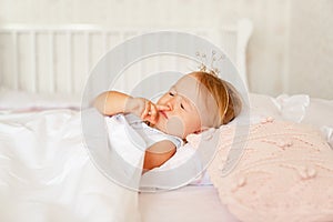 Little girl sleeping in bed in bedroom with crown. Princess birthday party.