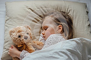 Little girl sleeping in bed embracing soft toy at home