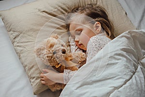 Little girl sleeping in bed embracing soft toy at home
