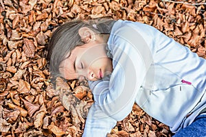 Little girl sleeping on the bed of laves in national park Biogradska Gora in autumn, Montenegro