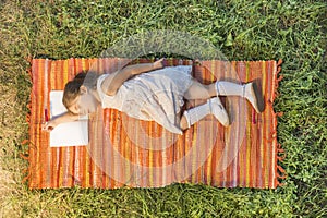 Little girl sleeping on the opened notebook lying down on the picnic blanket