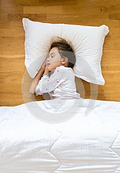 Little girl sleeping on wooden floor on white pillow