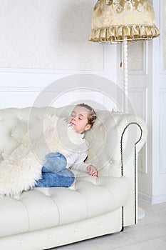 Little girl sleeps under white skin on white sofa photo