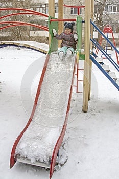 A little girl slides down a slide on a playground in winter.