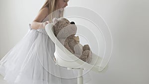 A little girl in a smart dress plays with a teddy bear