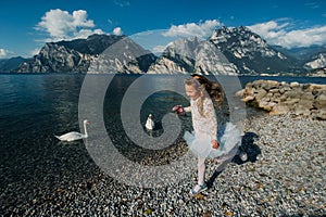 A little girl in a smart white dress walks along the embankment of lake Garda.A girl is photographed against the background of a