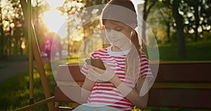 Little girl with a smartphone at sunset outdoors