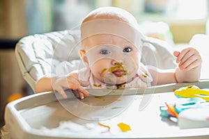 little girl with smeared face in broccoli puree. first lure of child. Healthy food for children up to year