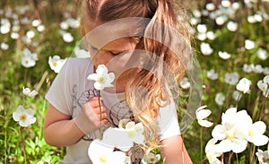 Little girl smelling anemone flower. Summer meadow.  Happy child enjoying nature outdoors