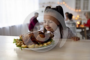 Little girl smelling yummy roasted turkey, having festive Thanksgiving or Christmas dinner with family in dining room