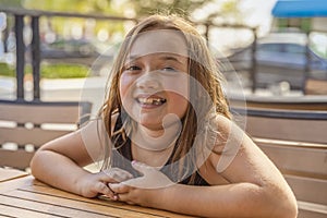 A little girl smiles at the camera while sitting at a table outside on a cafe patio