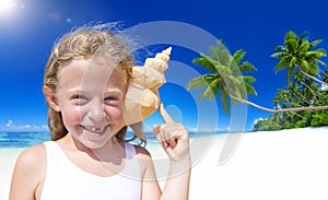 Little Girl Smiling at Camera by the Beach with Seashell Against her Ears