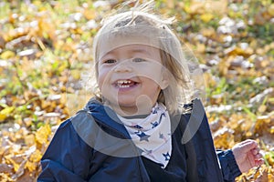 A little girl smiling happily sitting in the autumn leaves, leaf fall-a joyful time.