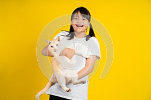Little girl smiling and happy, She is holding a cat in a studio isolated on yellow background