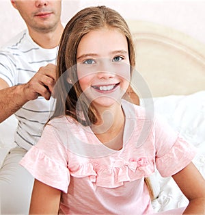 Little girl is smiling while her father is combing daughter`s hair