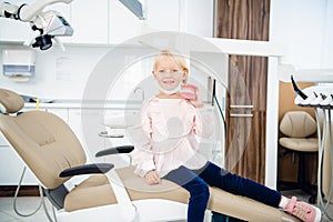 Little girl smiling and playing with dentures, in the dental office