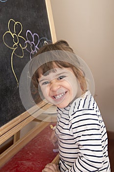 Little girl smiling proud of her drawing of flowers on blackboard