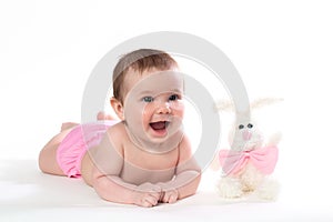 Little girl smiling with a toy rabbit lies on white background.