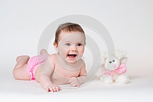 Little girl smiling with a toy rabbit lies on white background.