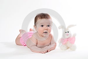 Little girl smiling with a toy rabbit lies on white background.