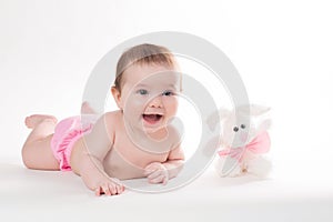 Little girl smiling with a toy rabbit lies on white background.
